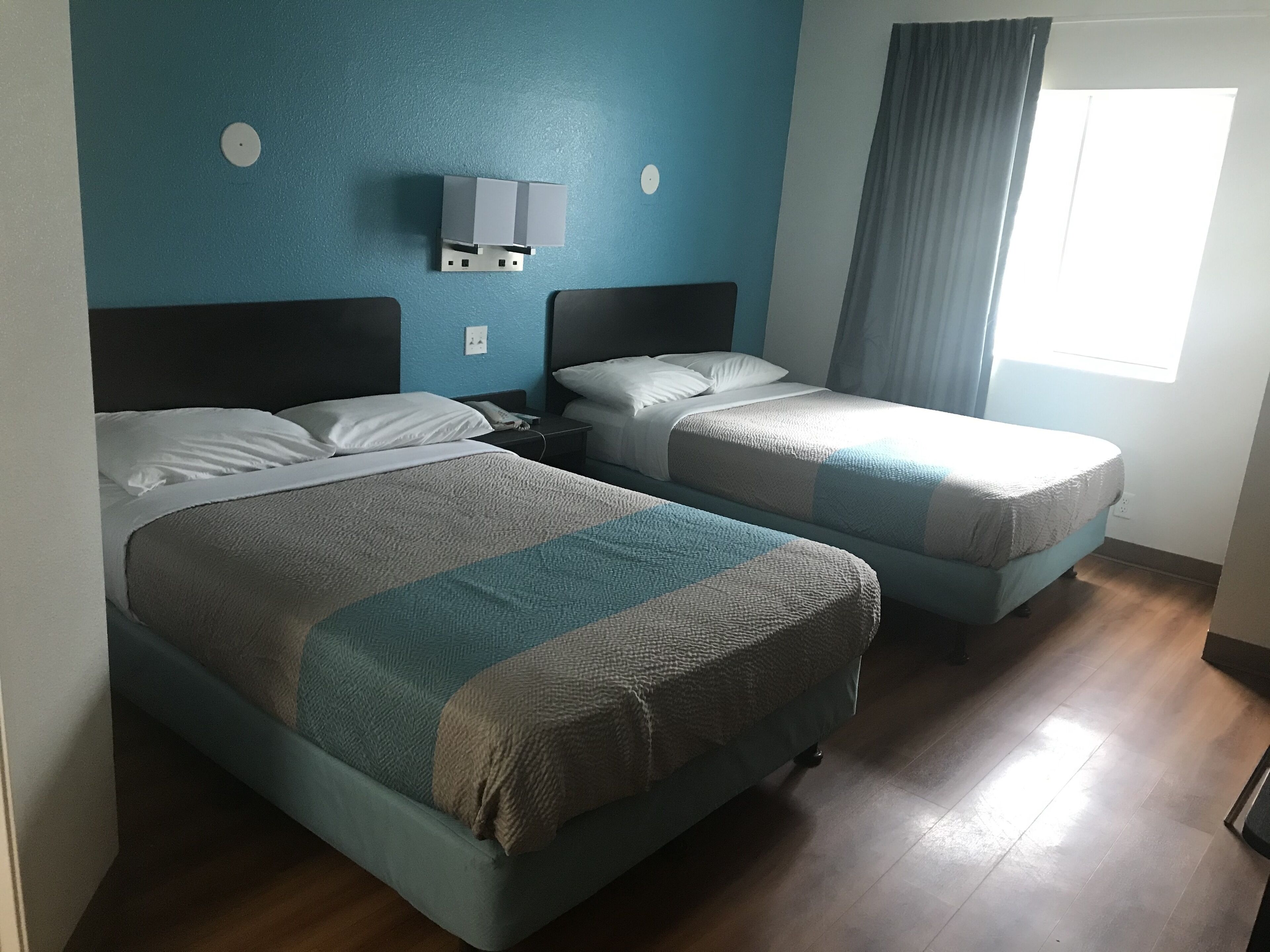 Een hotelkamer met twee bedden, een nachtkastje, een wandlamp en een raam met gordijnen.
