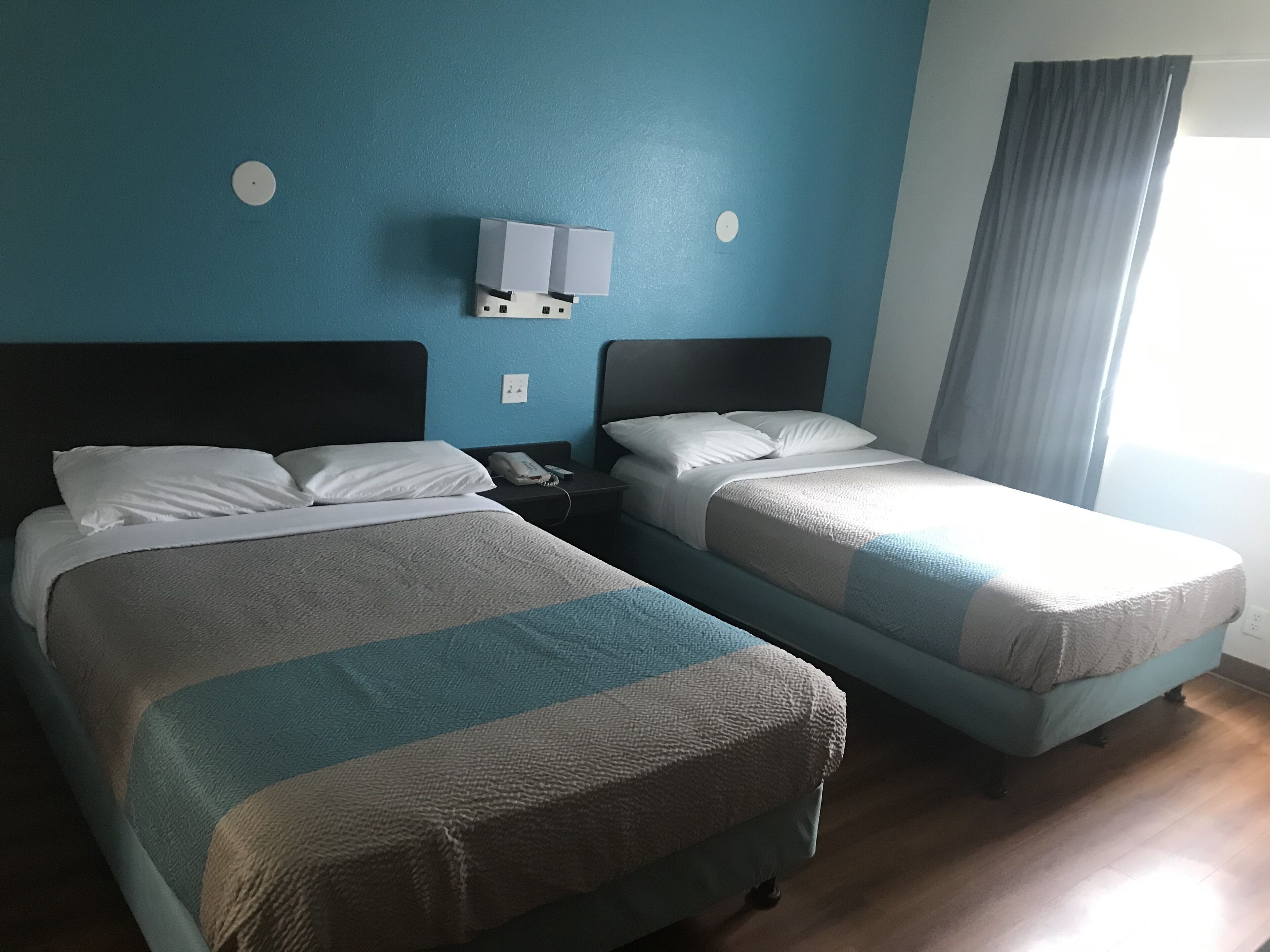 A hotel room with two beds, a nightstand, a phone, and a wall-mounted light fixture.