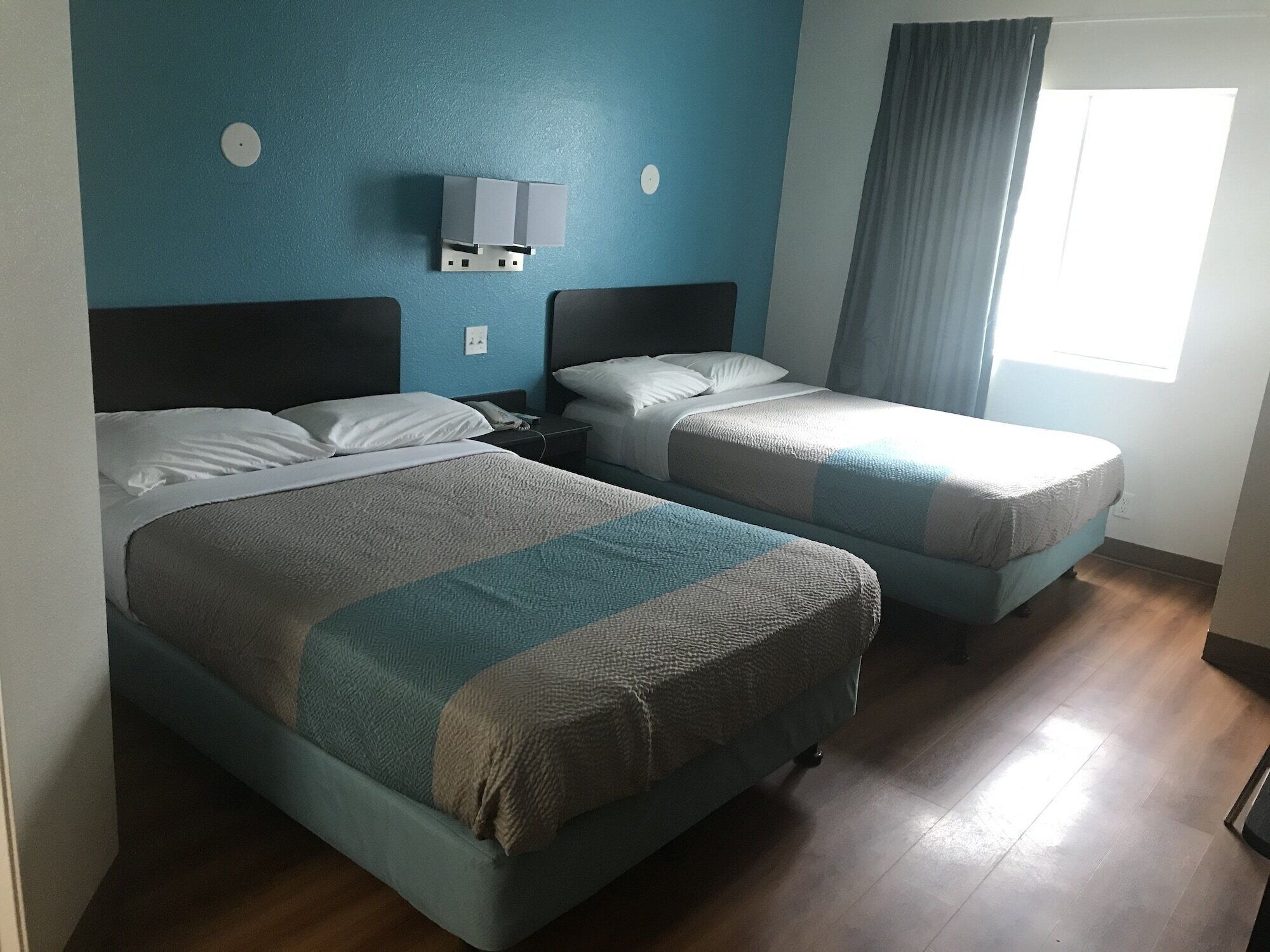 Ein Hotelzimmer mit zwei Betten, einem Nachttisch, einer Wandlampe und einem Fenster mit Vorhängen.