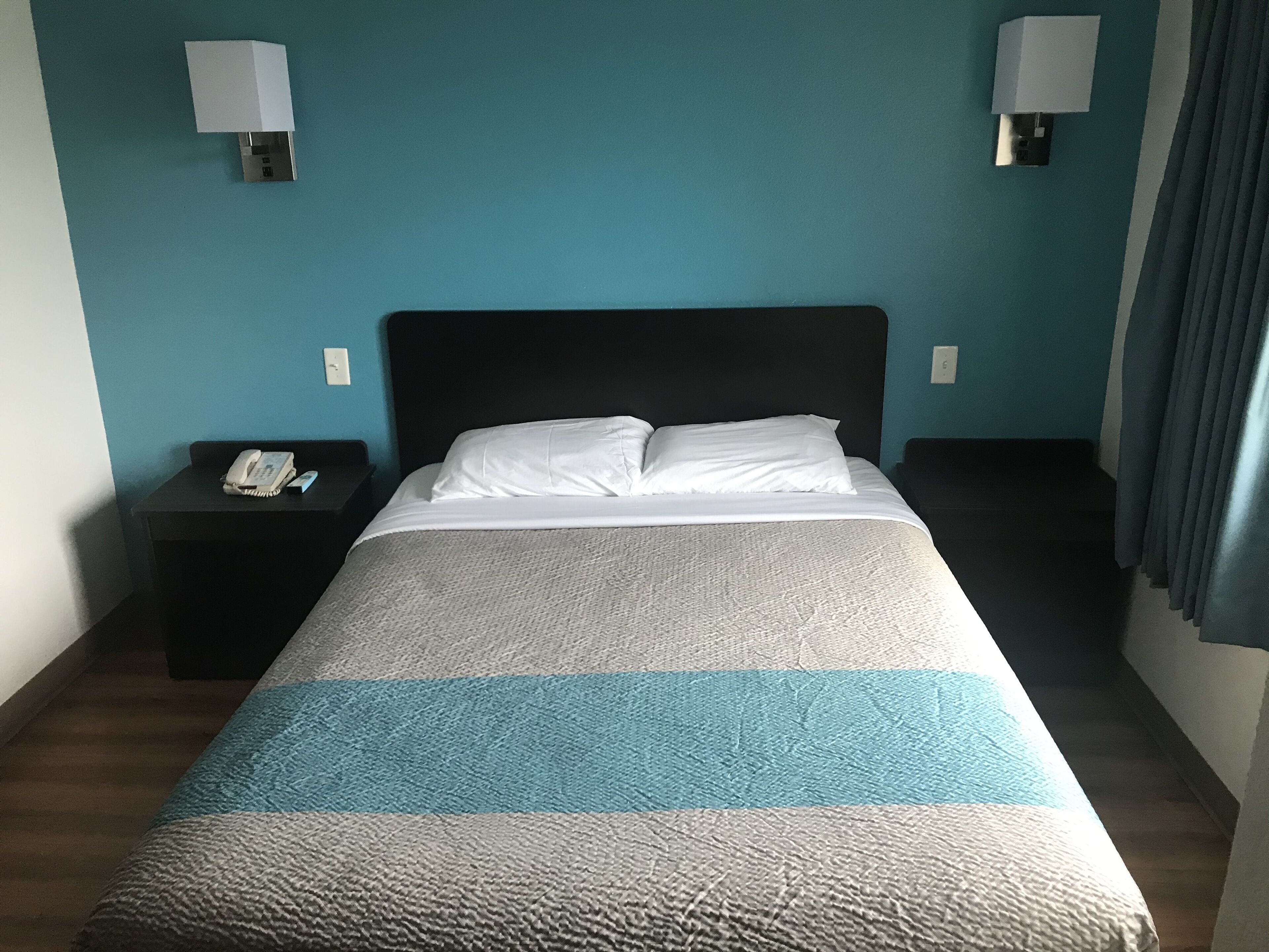 A hotel room with a bed, two bedside tables, a telephone, and wall-mounted lamps.