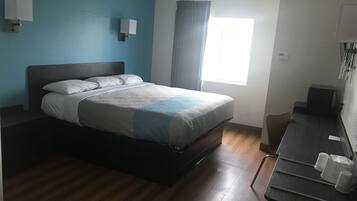 A hotel room with a bed, a desk with a chair, a window with curtains, and wall-mounted lamps.