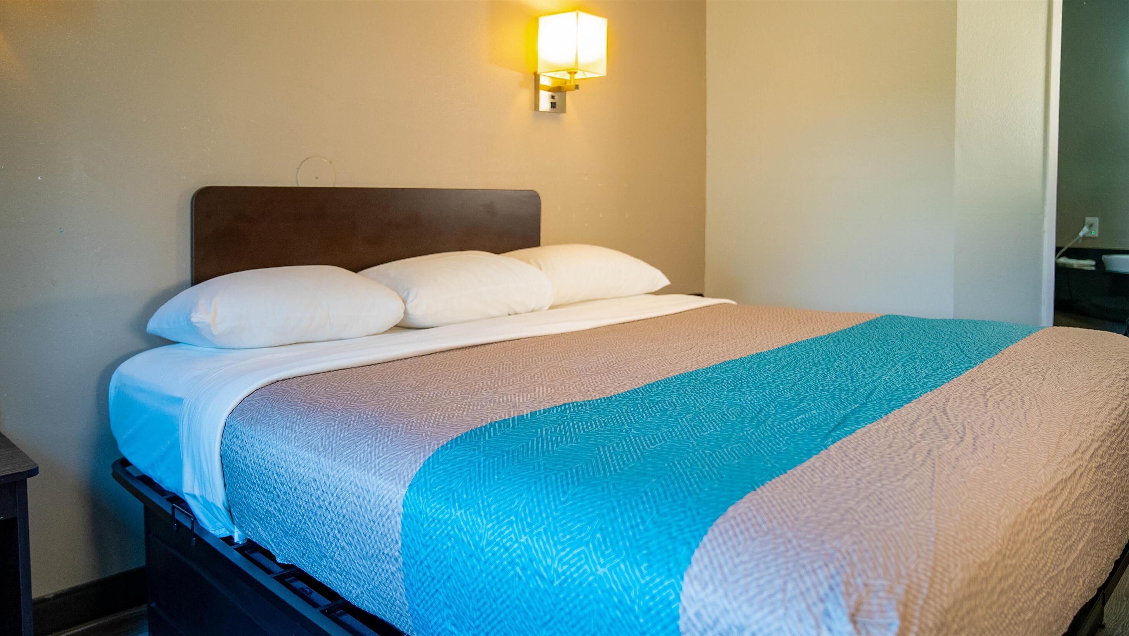 A neatly made bed with white and blue bedding, a wall-mounted lamp, and a dark headboard.