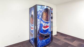 A vending machine with a Pepsi logo, located in a room with a carpeted floor and white walls.