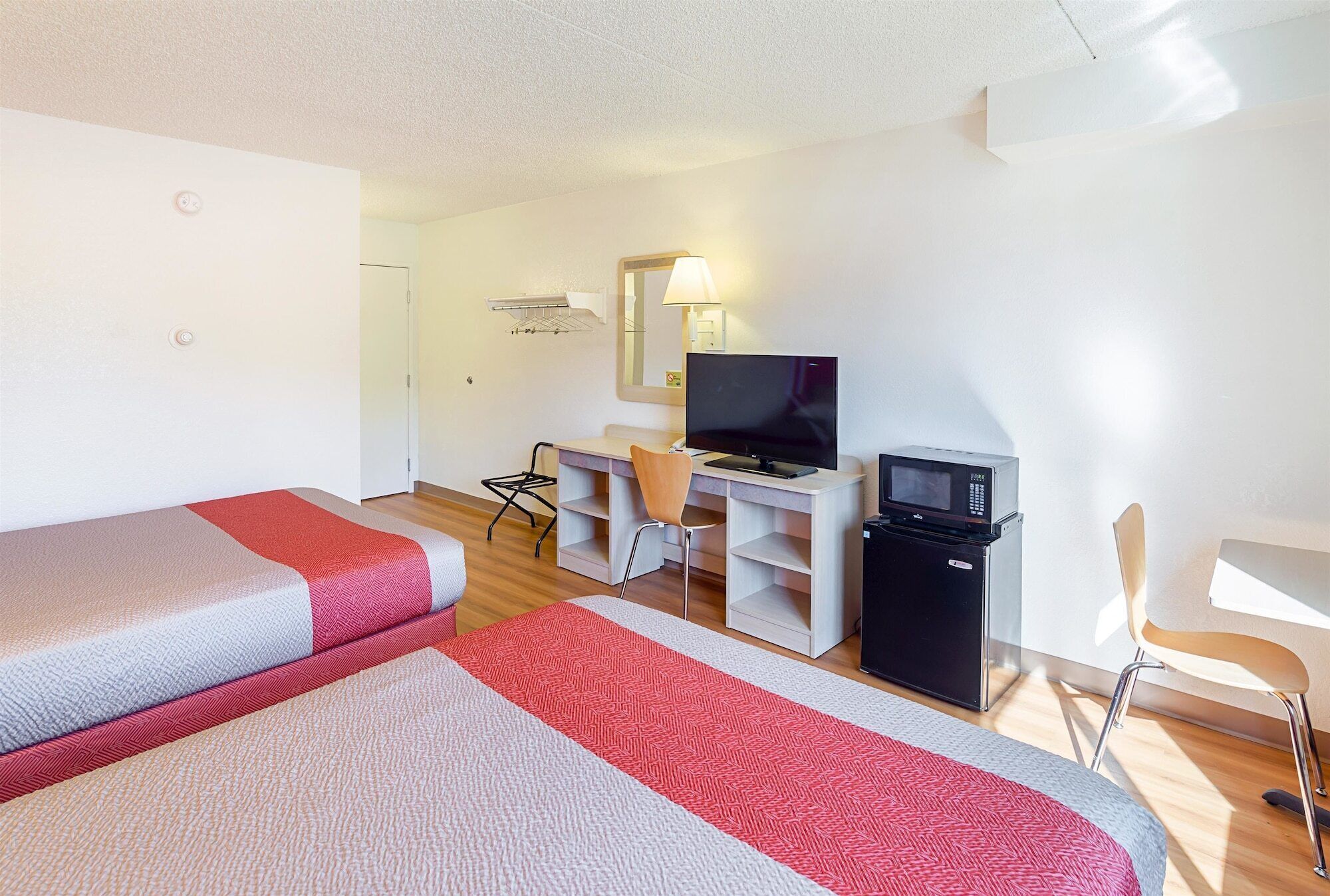 A hotel room with two beds, a desk with a TV, a microwave, and a chair.