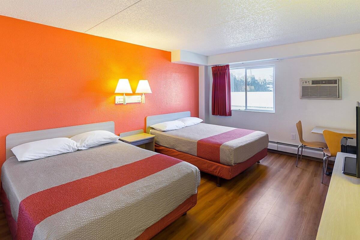Habitación de hotel con dos camas, un escritorio y una silla. Hay dos lámparas de pared y una ventana con cortinas.