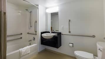 A bathroom with a bathtub, a sink, a toilet, and handrails.