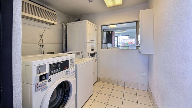 A laundry room with a front-loading washer and dryer, a ventilation hood, and a window with a view of the outside. - Motel 6 Laredo, TX - South (Laredo)