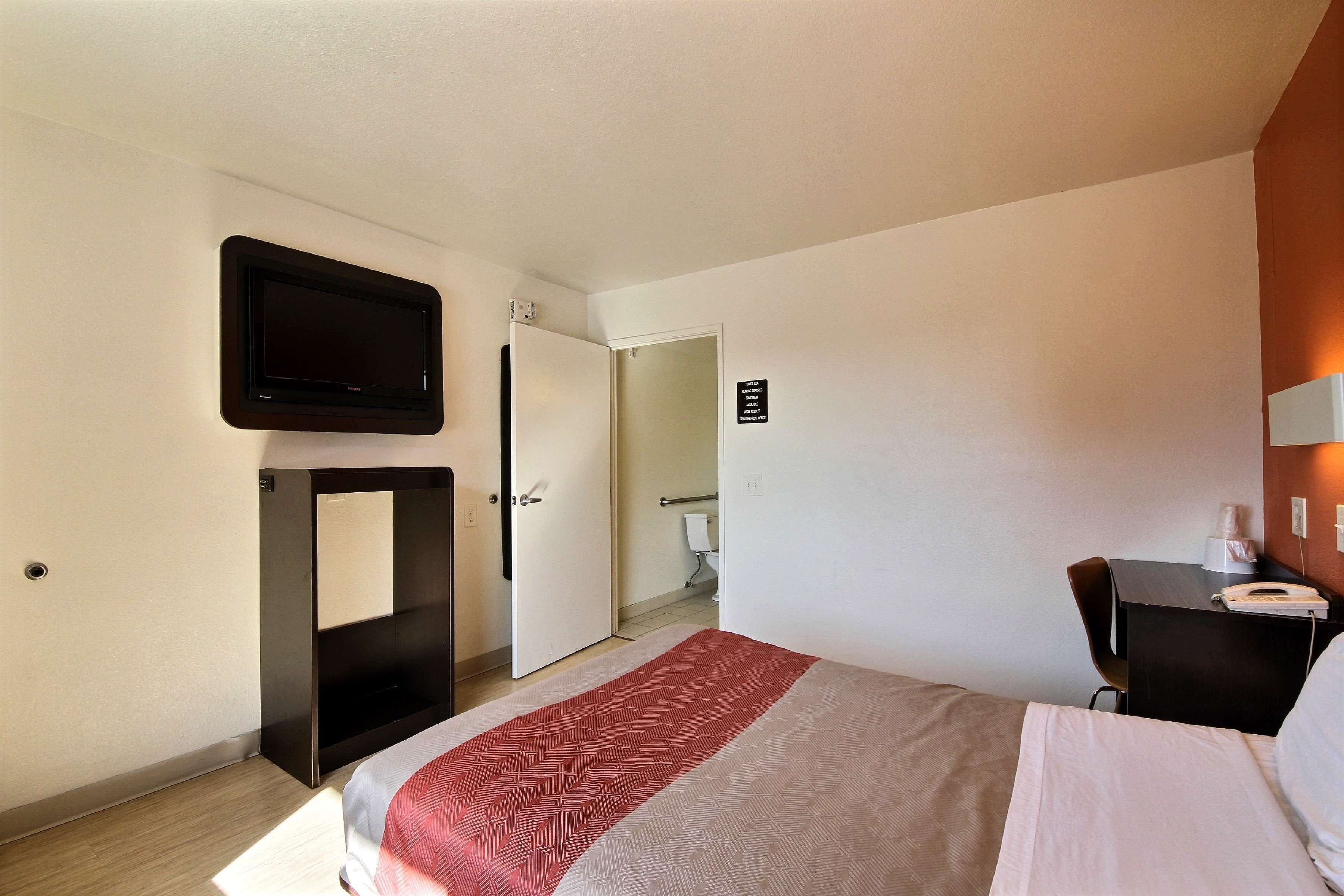 Une chambre d’hôtel comprenant un lit, un bureau avec un téléphone, un téléviseur fixé au mur et une porte donnant accès à une salle de bain.