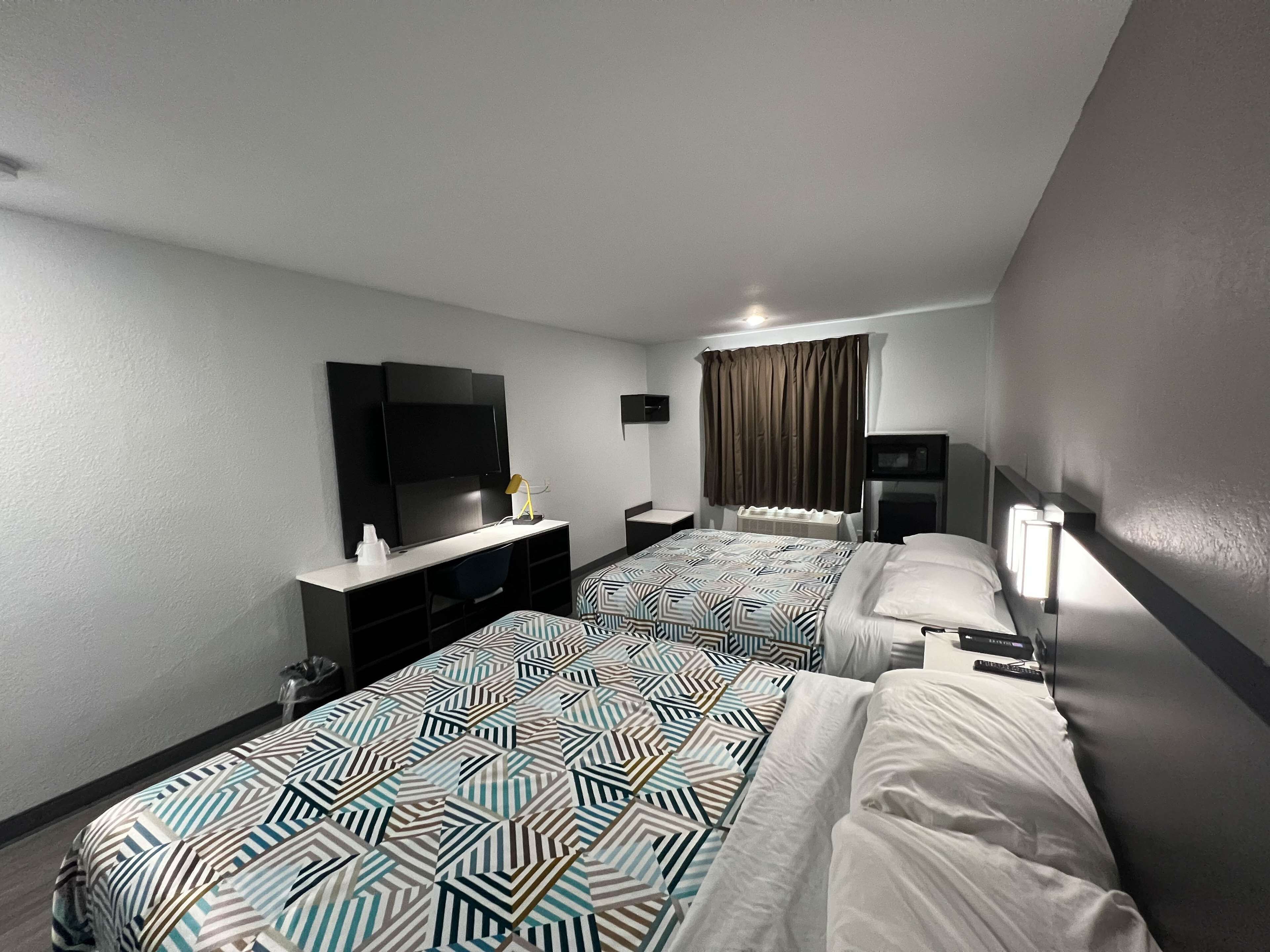 A hotel room with two beds, a TV, a desk, and a window with curtains.