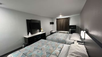 A hotel room with two beds, a TV, a desk, and a window with curtains.