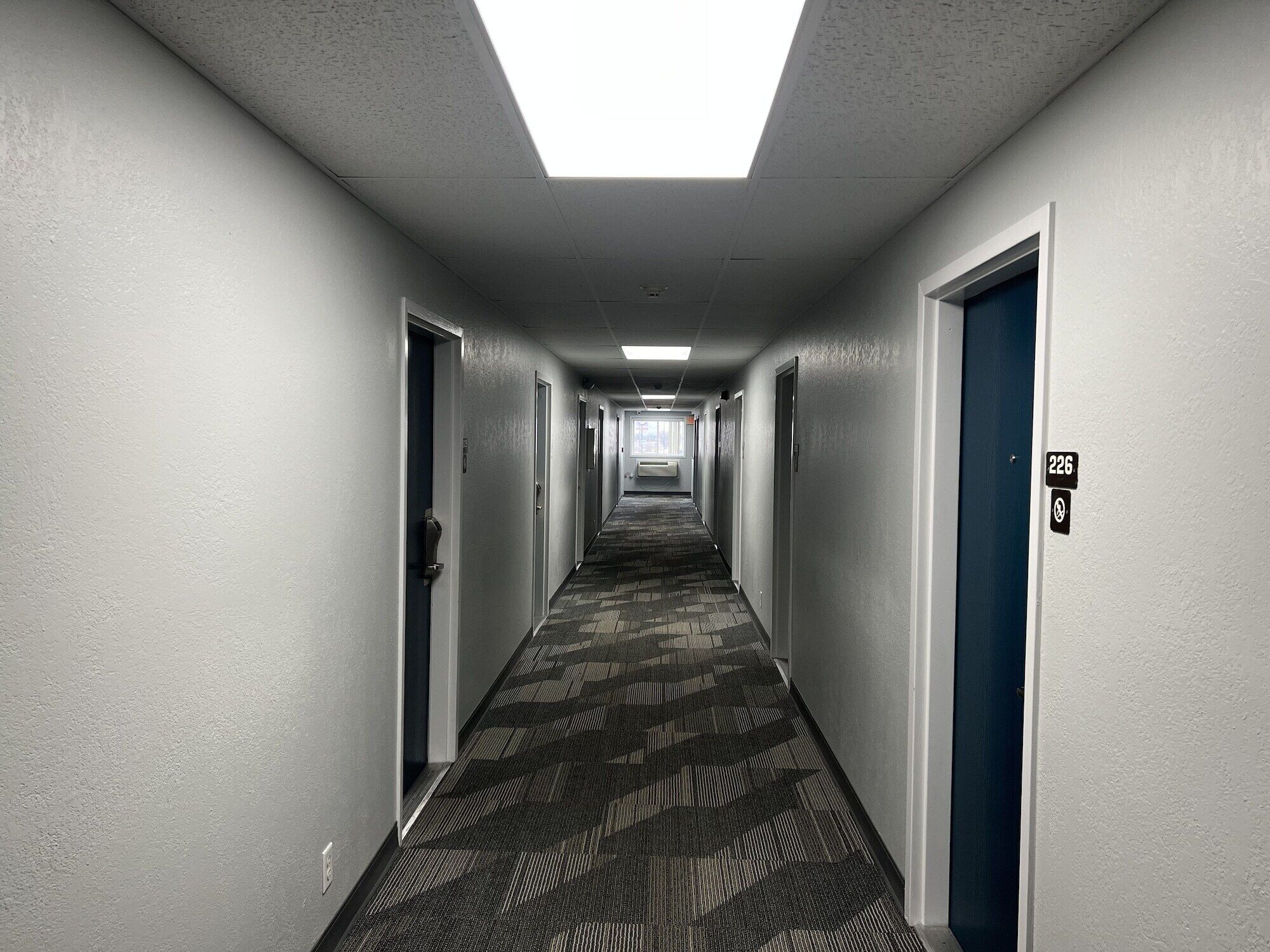 Un largo pasillo de hotel, estrecho, con pisos alfombrados y puertas a ambos lados.