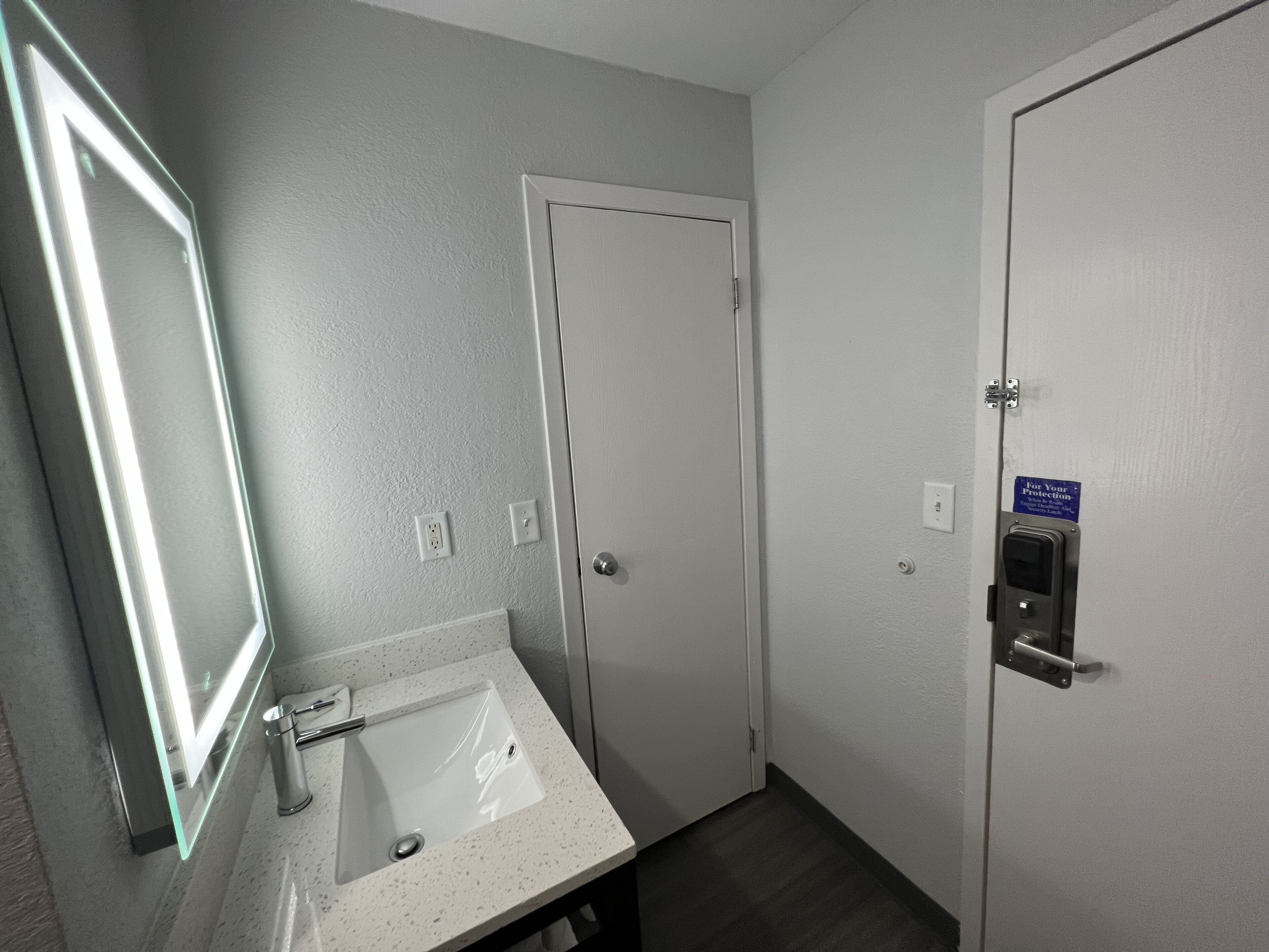 Une salle de bain équipée d’un lavabo, d’un miroir et d’une porte dotée d’une serrure de sécurité.