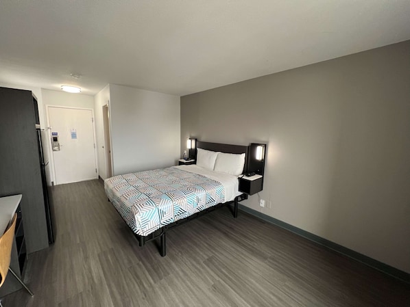 A hotel room with a bed, bedside tables, a desk, and a door.