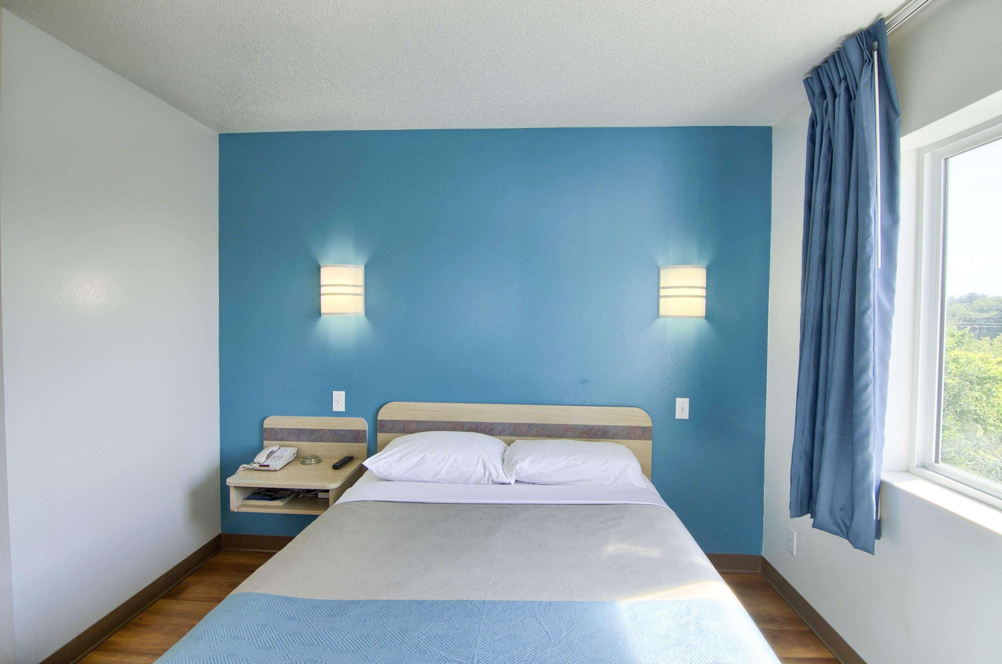 Un dormitorio con cama, mesita de noche, lámpara y ventana con cortinas.