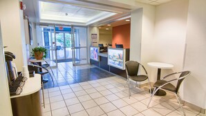 A reception area with a desk, chairs, a small table, a potted plant, and a sign indicating an exit.