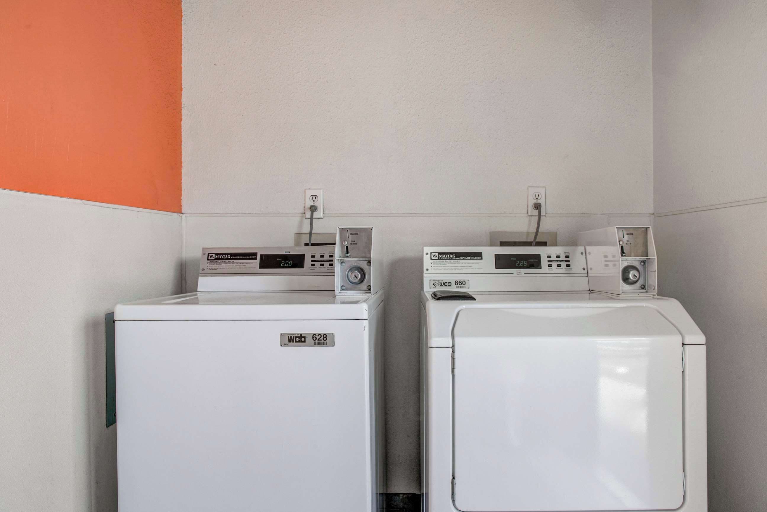 Two front-loading washing machines in a laundry room with a plain wall and a corner painted orange.