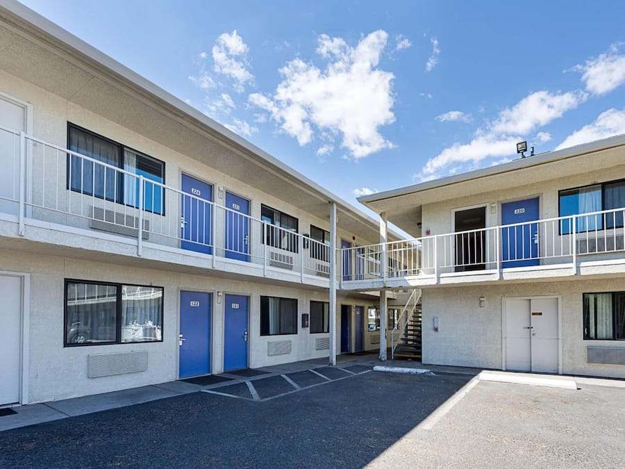 A multi-story motel with a central courtyard, featuring a two-story structure with balconies, and a parking area in front.