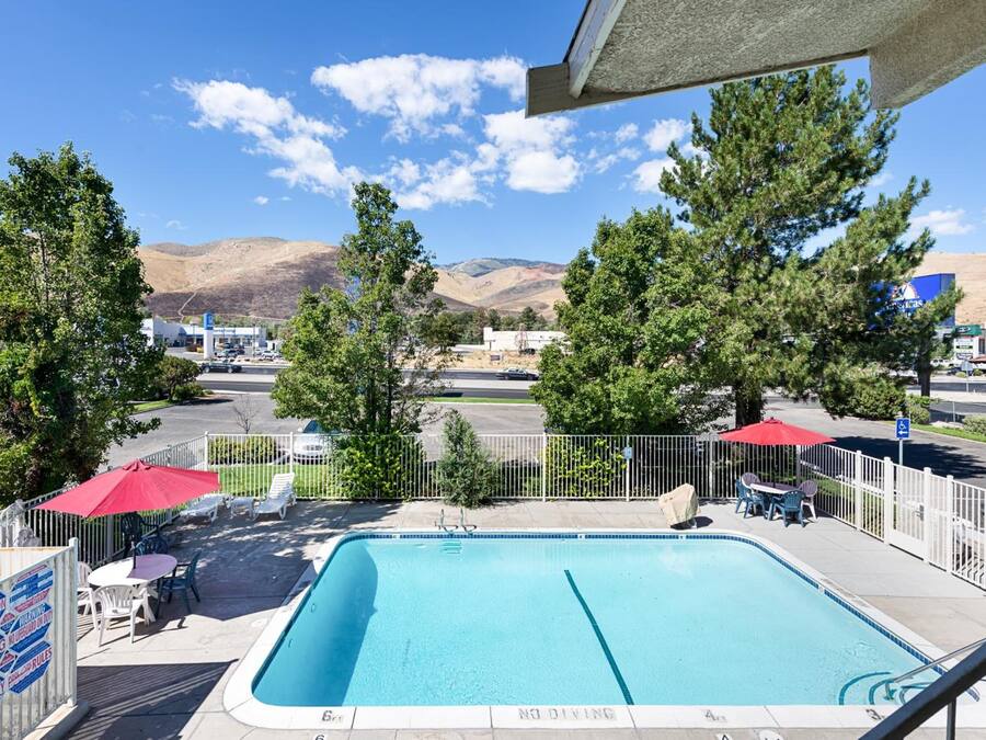 A swimming pool with a 'NO DIVING' sign, surrounded by a fenced area with lounge chairs and umbrellas, set against a backdrop of mountains and a clear sky.