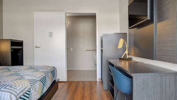 A hotel room with a bed, a desk, a chair, a TV, and a door leading to a bathroom.