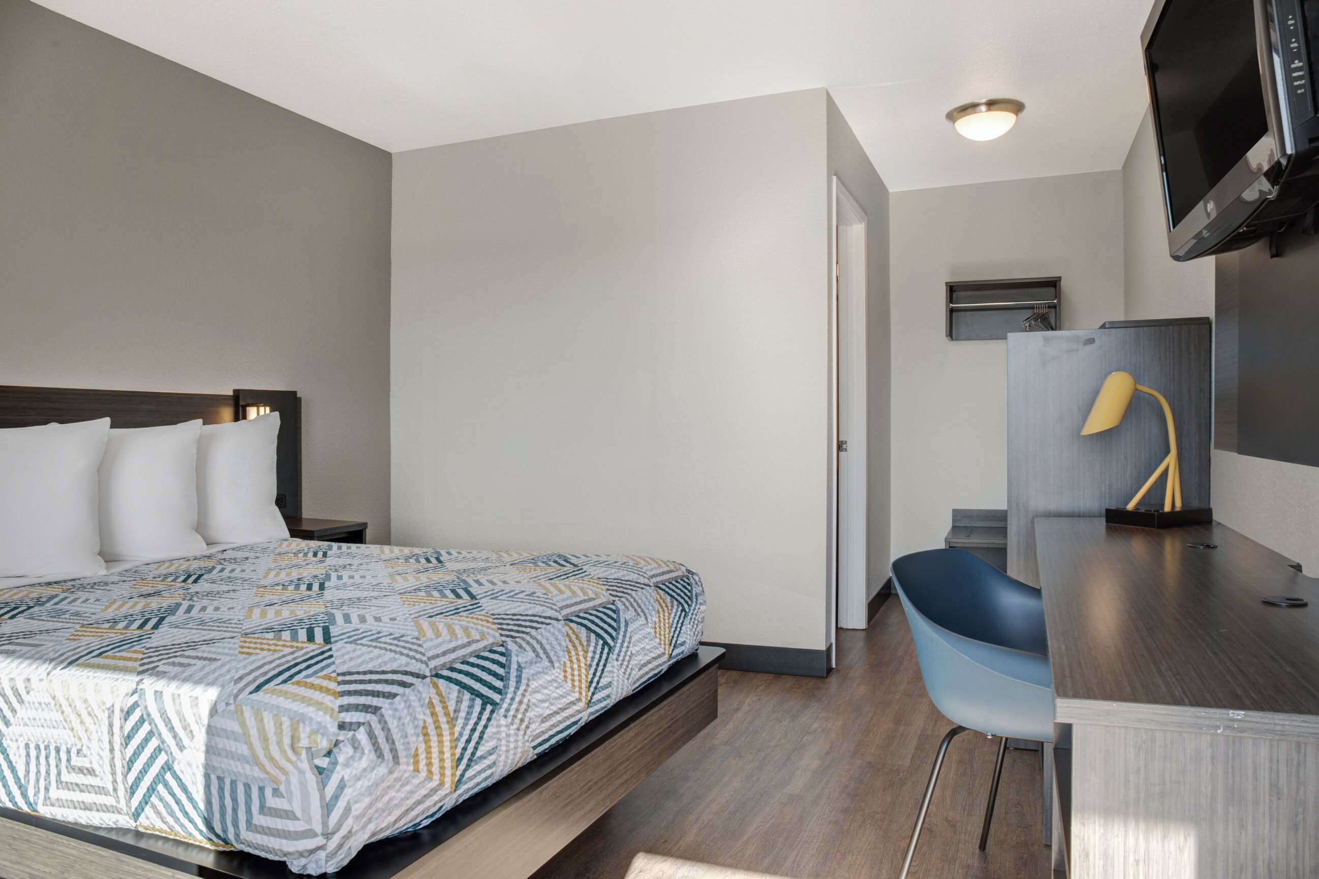 A hotel room with a bed, a desk, a chair, a television, and a small shelf.