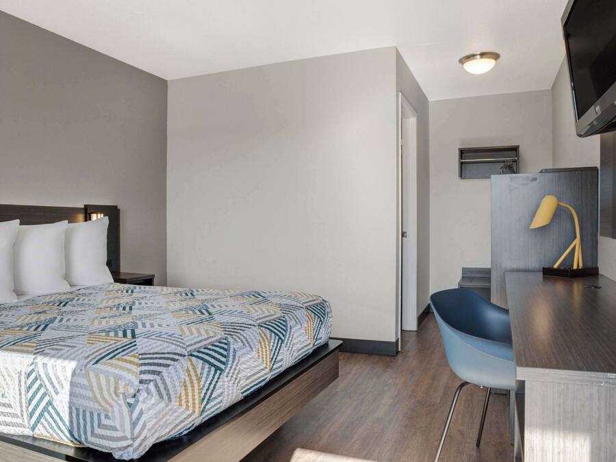A hotel room with a bed, a desk, a chair, a television, and a small shelf.