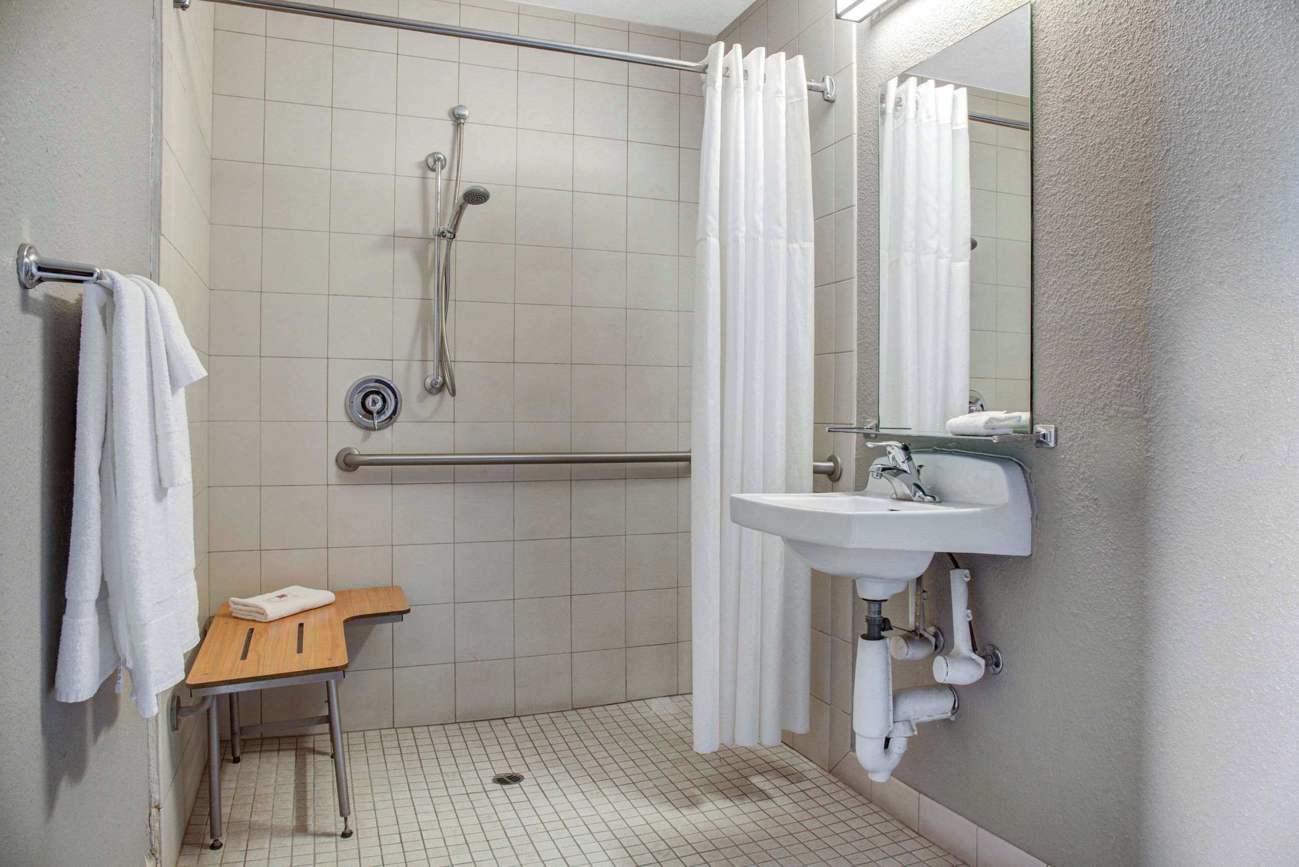 Une salle de bain avec une douche, un lavabo, un miroir et un petit tabouret en bois.