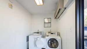 A laundry room with two washing machines and a dryer, a fire alarm, and an air conditioning unit on the wall. - Motel 6 Carson City, NV (Carson City)