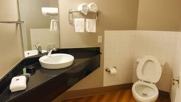 A bathroom with a black countertop sink, a mirror, a towel rack with towels, and a toilet.