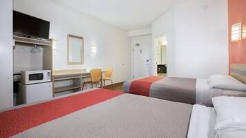 A hotel room with two beds, a desk with a microwave, a chair, and a television.