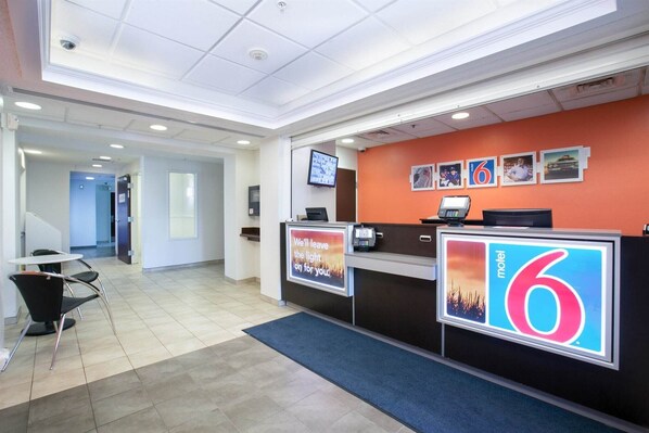 A hotel reception area with a modern design, featuring a reception desk, a digital screen, and a wall-mounted TV. - Motel 6 Brooklyn Center, MN - Minneapolis (Brooklyn Center)
