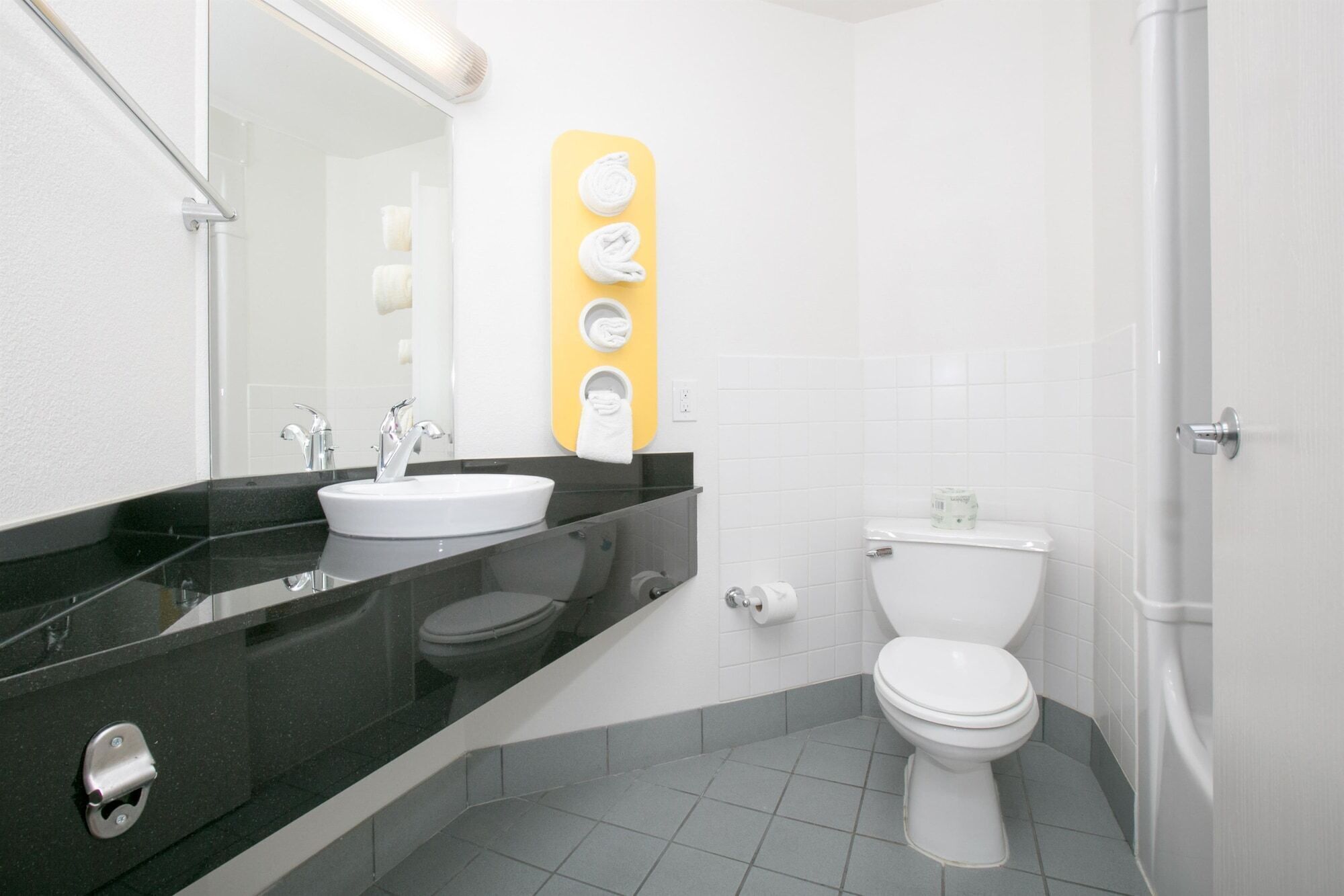 Une salle de bain moderne avec un plan de toilette noir, un lavabo blanc et des toilettes. Un porte-serviettes jaune est fixé au mur.
