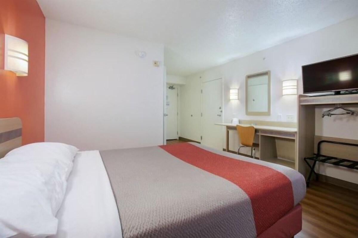 A hotel room with a bed, a desk, a chair, a television, and a wardrobe.