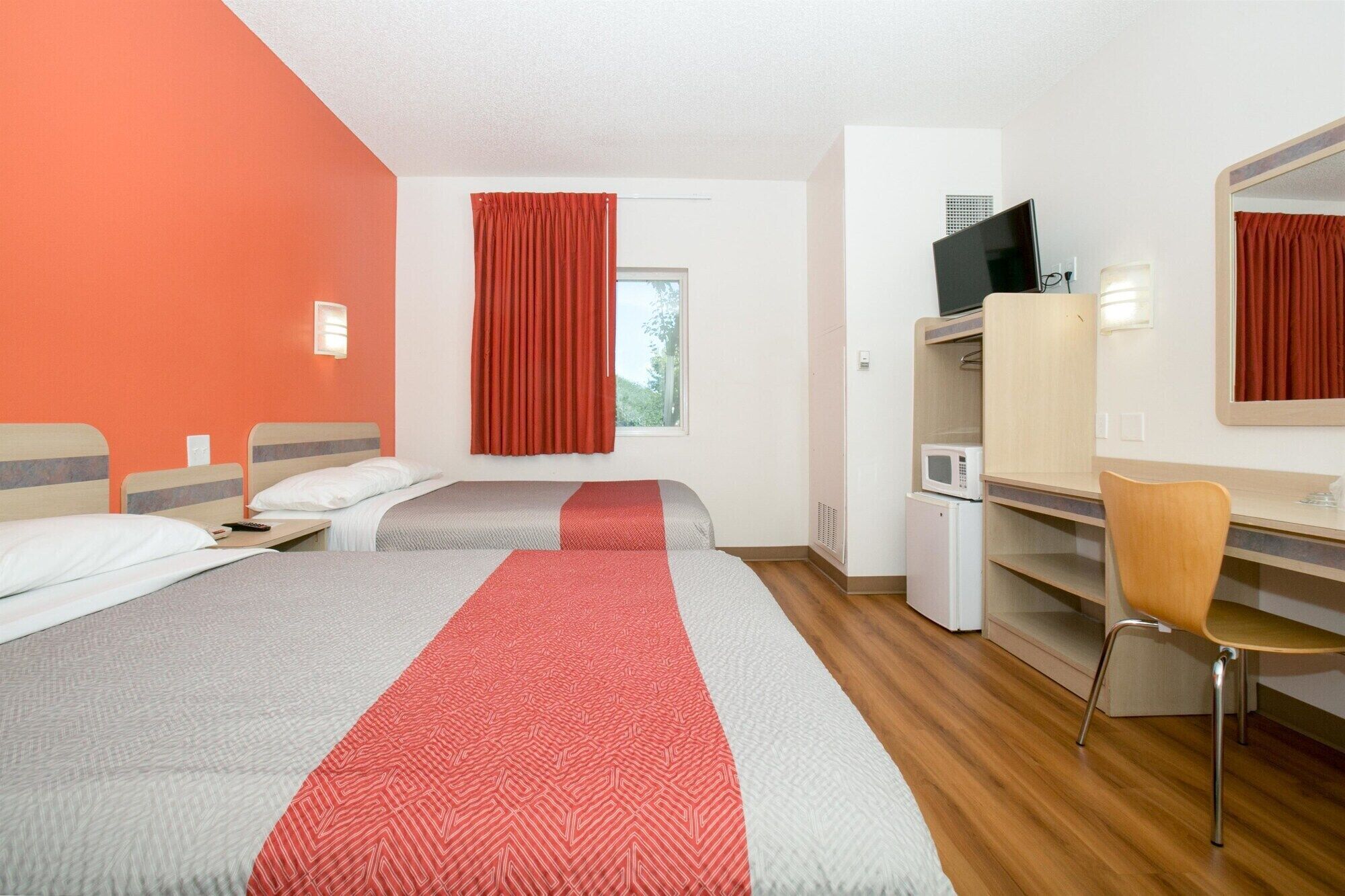 A hotel room with two beds, a desk, a chair, a microwave, and a television.