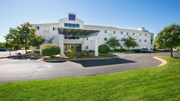 A large, modern hotel with a prominent '6' sign, featuring a covered entrance, multiple windows, and a well-maintained lawn.