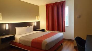Une chambre d’hôtel avec un lit, des tables de chevet, un bureau et une fenêtre avec des rideaux.