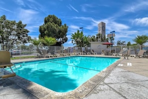 A swimming pool with lounge chairs and a tall building in the background. - Motel 6 Westminster South - Long Beach (Westminster)
