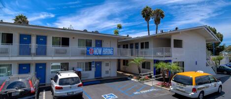 A motel with a 'NOW HIRING' sign, parking spaces, and a 'NO PARKING' sign.