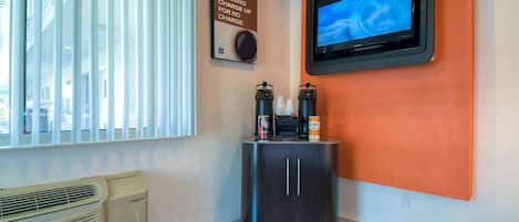 Ein Hotelzimmer mit an der Wand befestigtem Fernseher, einer Kaffeemaschine und einem Hinweis auf eine Gebühr für kostenlose Leistungen am Morgen.