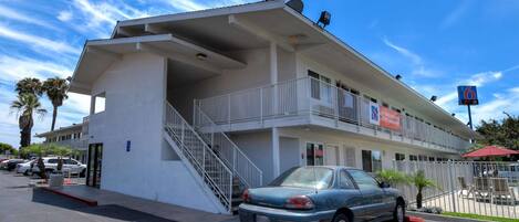 A two-story motel with a balcony on the second floor, a parking lot, and a clear blue sky.