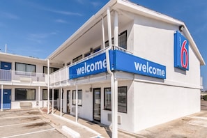 A motel with a 'Welcome' sign, a covered parking area, and a clear sky. - Motel 6 Fort Worth, TX - North (Fort Worth)