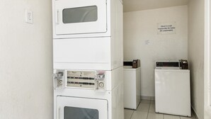 A laundry room with stacked washers and dryers, a sign stating 'Motel 6 is not responsible for items left unattended', and a small sign indicating laundry services. - Motel 6 Fort Worth, TX - North (Fort Worth)