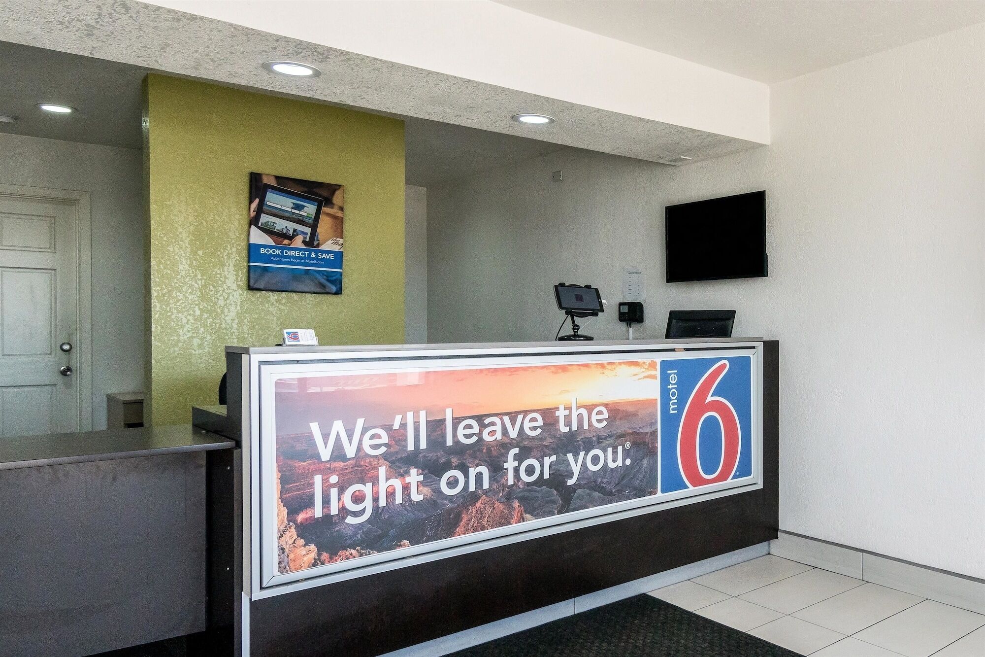 Een hotel receptiebalie met een groot bord waarop staat: 'We houden het licht voor je aan'.