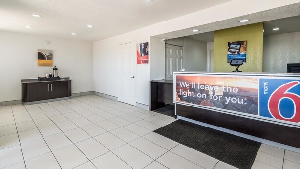 A hotel reception area with a tiled floor, a reception desk, a coffee machine, and a sign advertising the hotel. - Motel 6 Fort Worth, TX - North (Fort Worth)