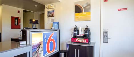 En hotellreception med en digital skärm, en kaffestation och en nödutgångsdörr.