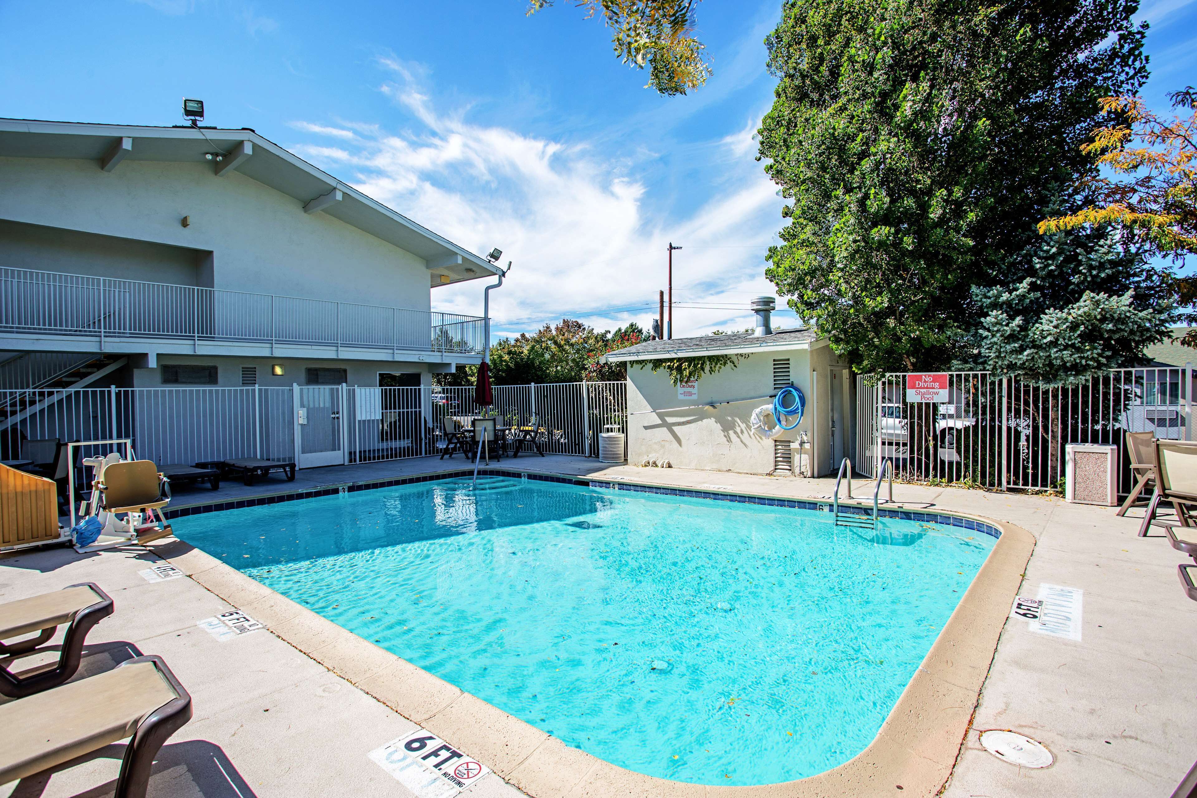 A rectangular swimming pool with a white fence, lounge chairs, and a building with a balcony in the background.