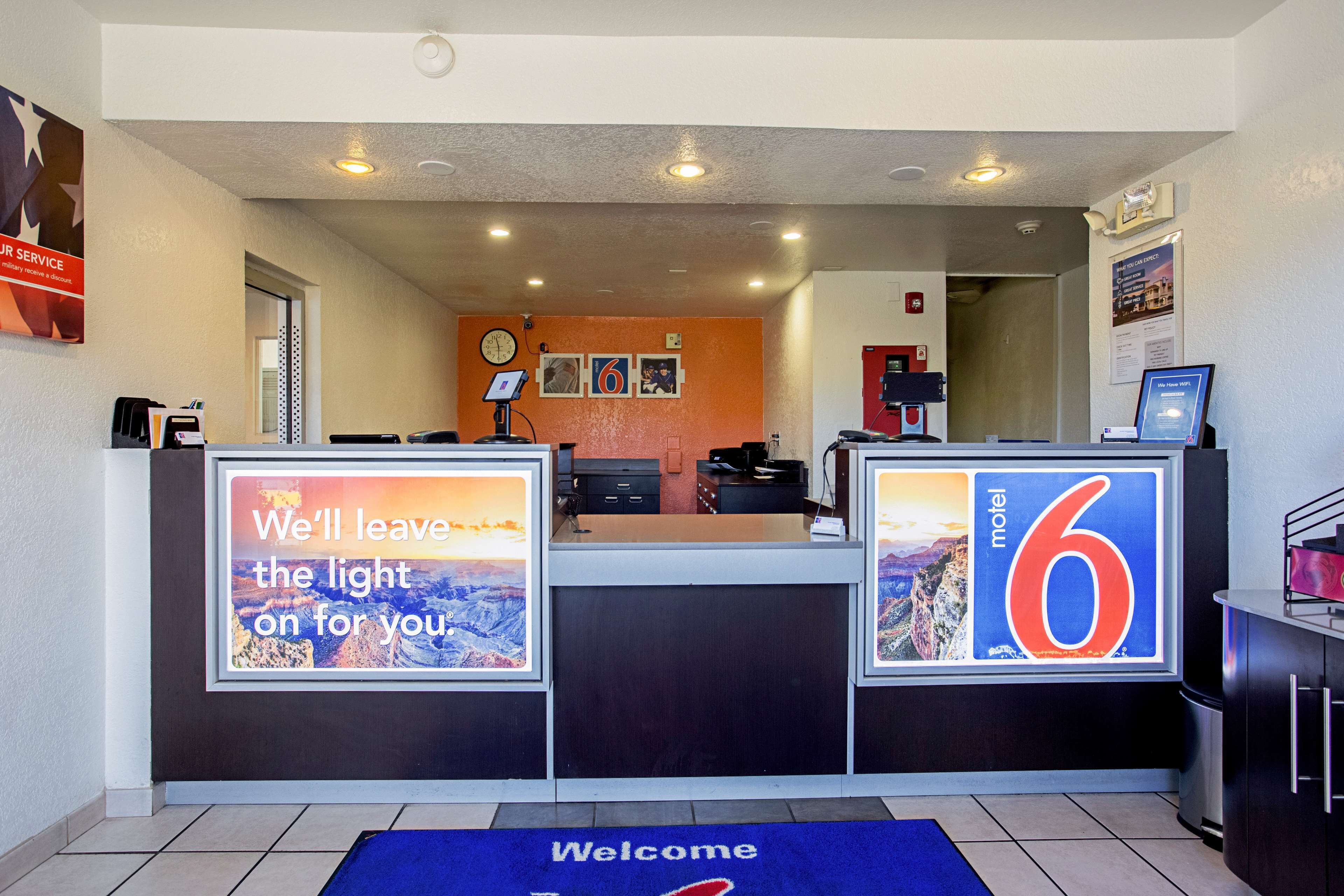 A hotel reception area with a reception desk, a clock, framed pictures on the wall, and a welcome mat.