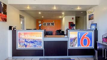A hotel reception area with a reception desk, a clock, framed pictures on the wall, and a welcome mat.