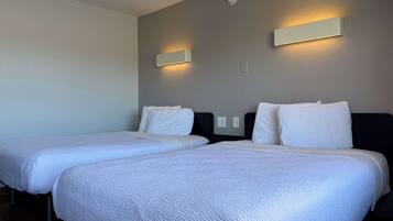 Une chambre d’hôtel avec deux lits simples, chacun doté de draps blancs et d’une tête de lit. Des appliques murales sont fixées de chaque côté des lits.