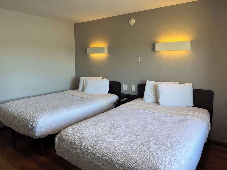 Een hotelkamer met twee bedden, elk met hoofdbord en wit beddengoed. Boven elk bed hangen wandlampen.