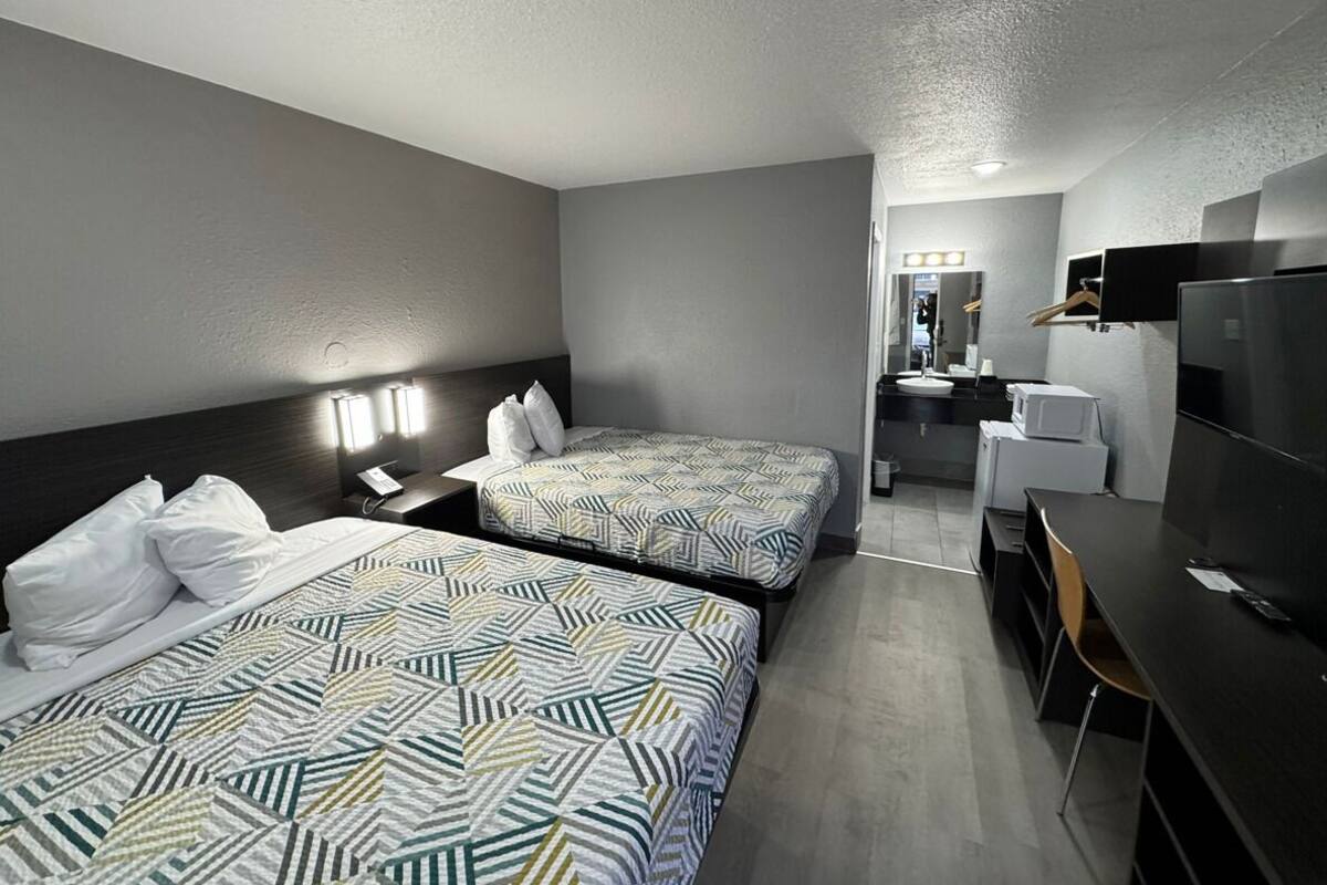 A hotel room with two beds, a desk, a chair, a TV, and a mirror.